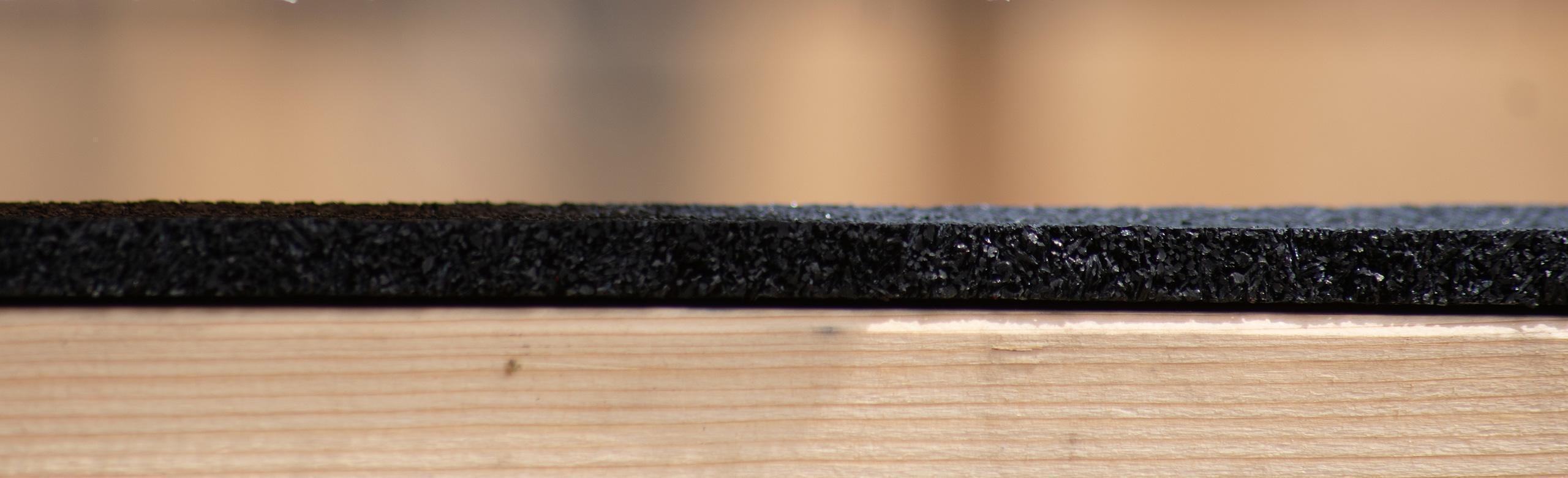 Rubber granulate mat on wood – insulation, flooring, recycled, construction Close-up of a black rubber granulate mat on light wood, shown from the side in cross-section.